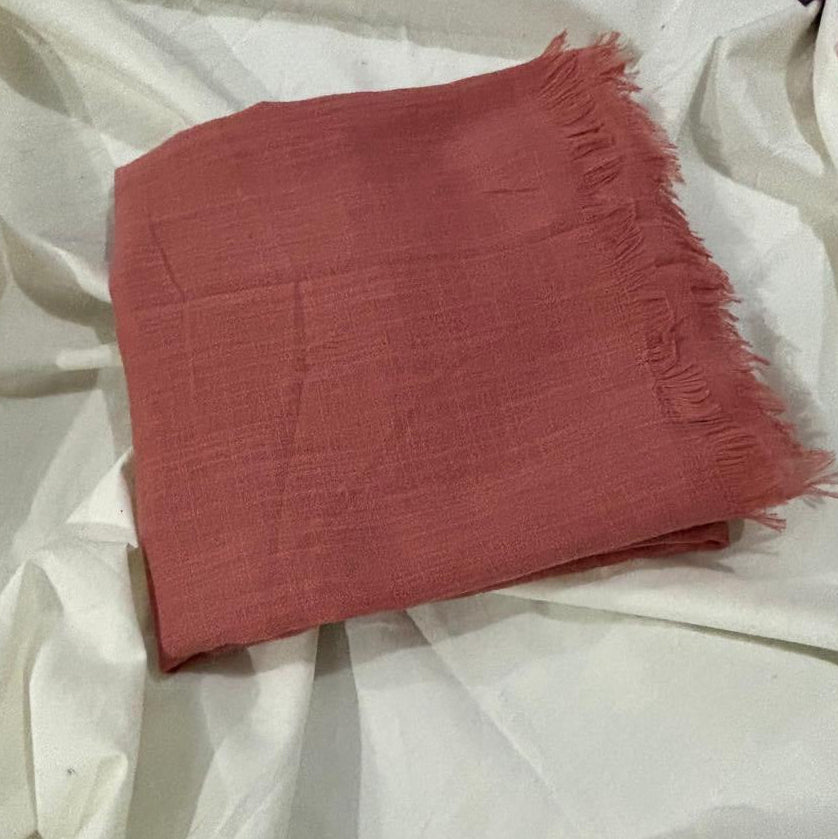 A folded dusty rose pink scarf with frayed edges