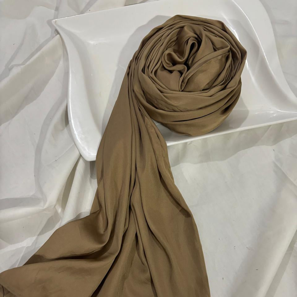 A matte gold scarf or shawl draped over a white ceramic dish on a white fabric background.