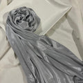 A shiny silver-gray fabric scarf or sash draped over a white rectangular tray on a white fabric surface.