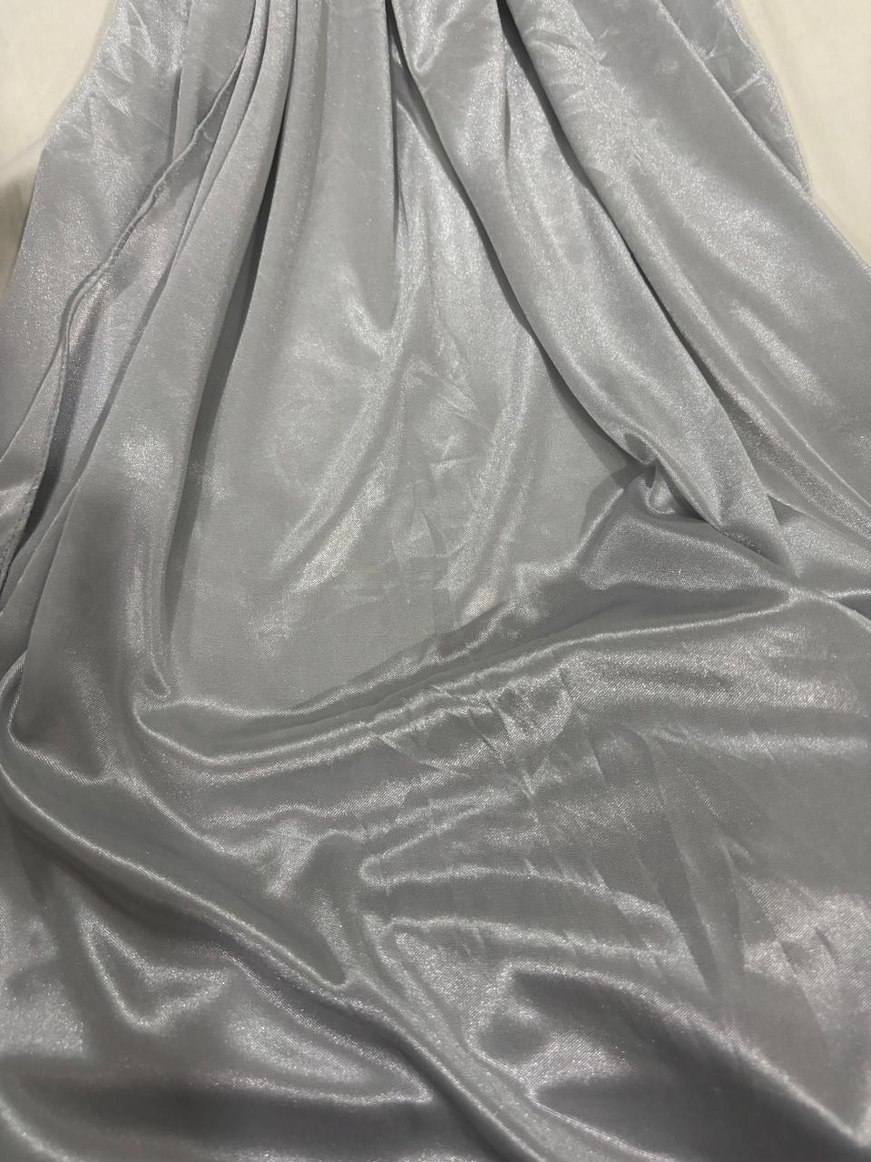 A close-up of draped shiny fabric in a light silver-gray color, showing soft folds and a satin-like sheen.