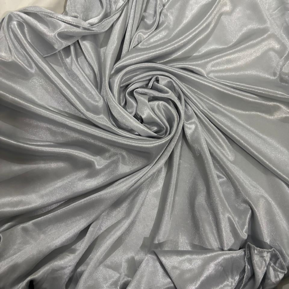 A close-up of shiny silver-gray fabric draped in a spiral pattern, showing its smooth, satin-like texture.